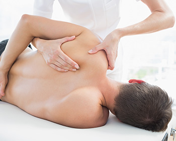 Professional female physiotherapist giving shoulder massage to m